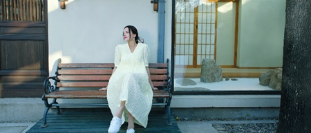 A person in a white dress sitting on a bench

Description automatically generated